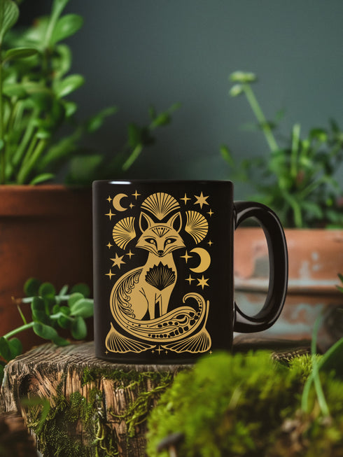 A black ceramic mug featuring a stylized golden fox design surrounded by Art Deco ginkgo fans, crescent moons, and stars. The mug has a glossy finish and ergonomic handle.